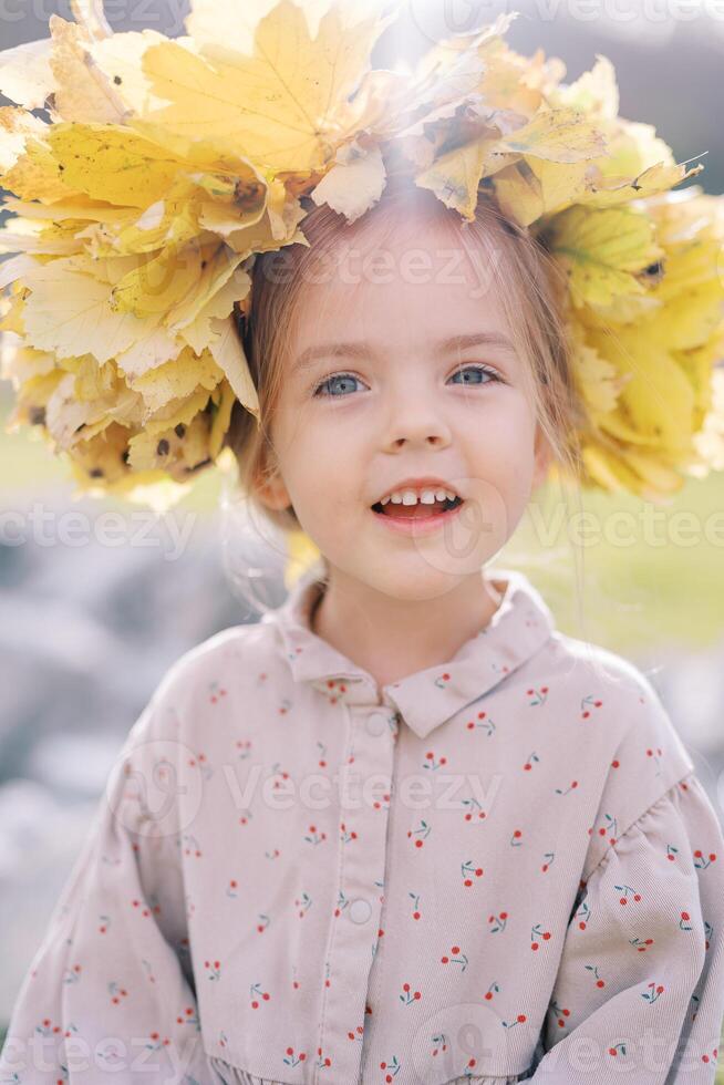 Little joyfully smiling girl wearing a wreath of yellow leaves. Portrait photo