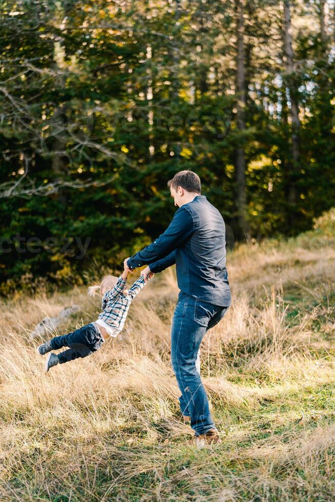 Dad is circling a little girl by the arms on a sunny lawn in the forest photo