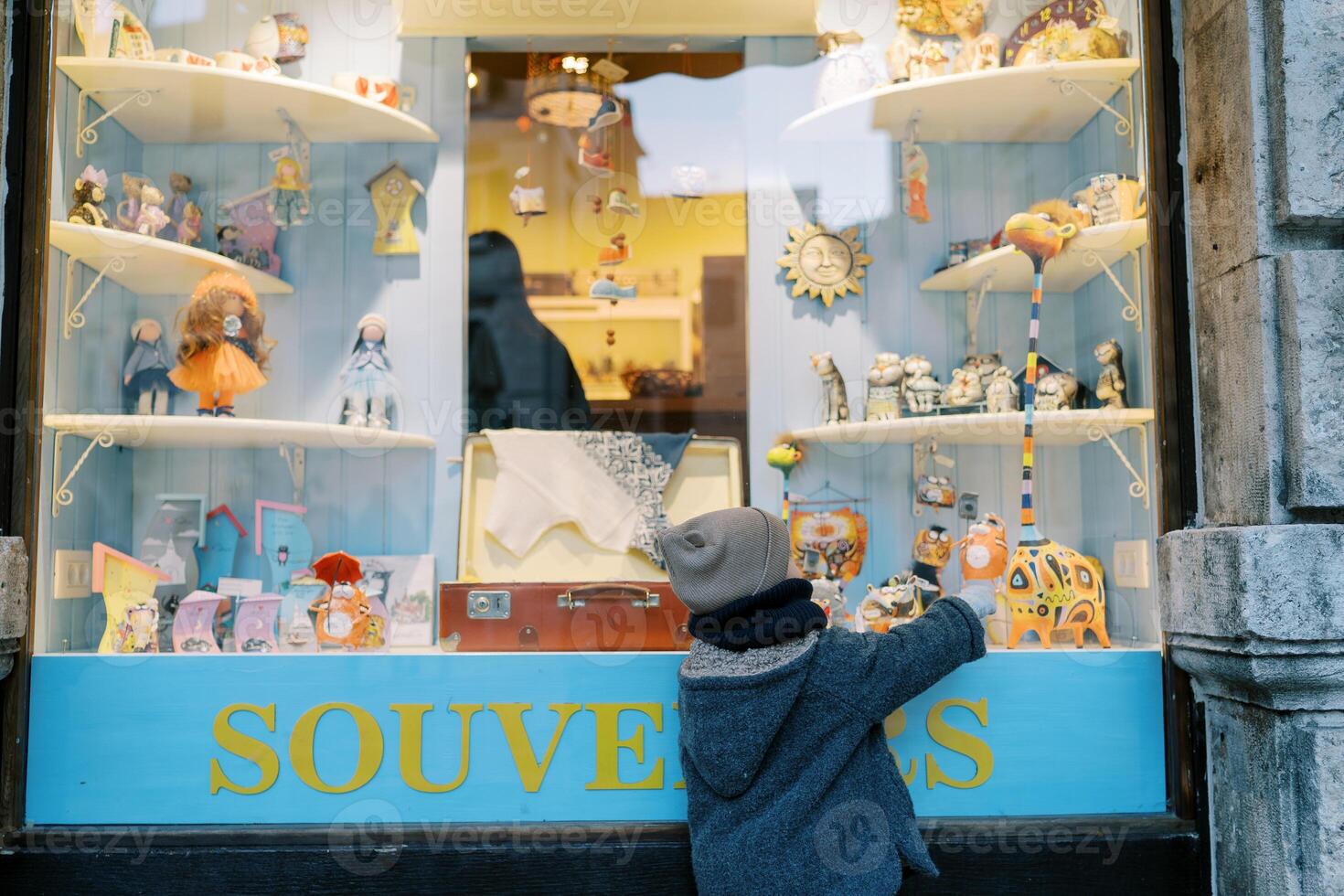 pequeño niña puntos a un vistoso jirafa figurilla en un regalo tienda ventana. espalda ver foto