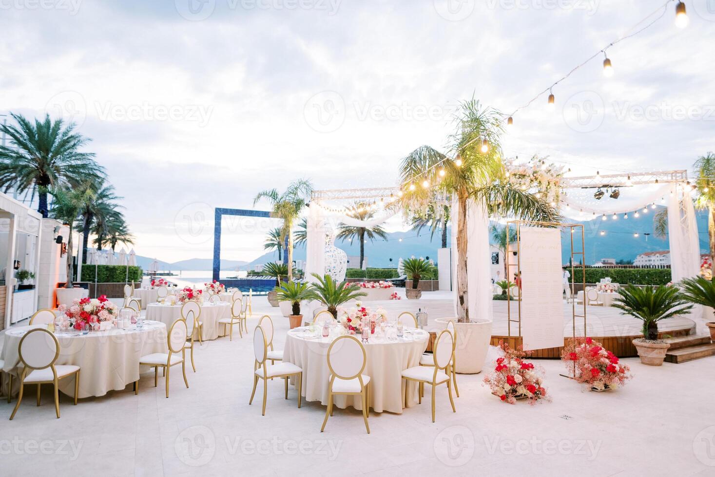 Covered festive tables with bouquets of flowers and garlands of light bulbs stand on the terrace photo