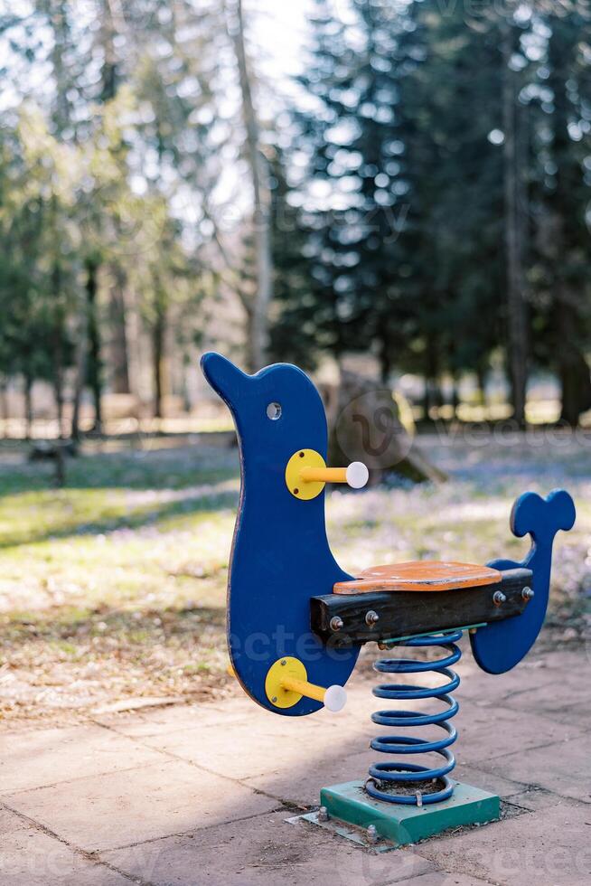 Spring swing with wooden handles stands on a rubber flooring in a playground photo