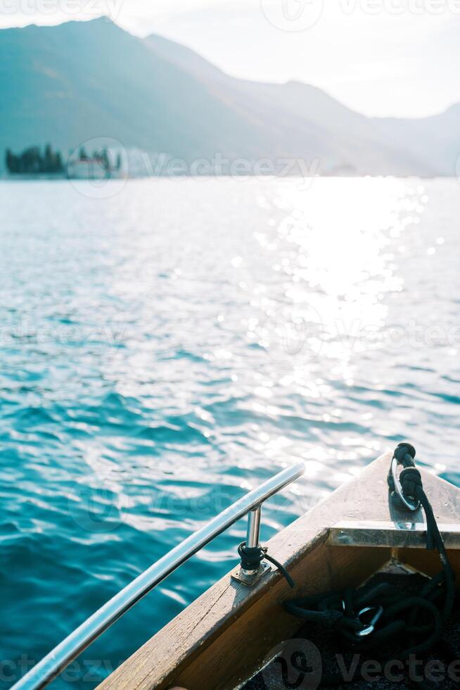 Bow of a wooden yacht sailing across the sparkling sea towards the mountains photo