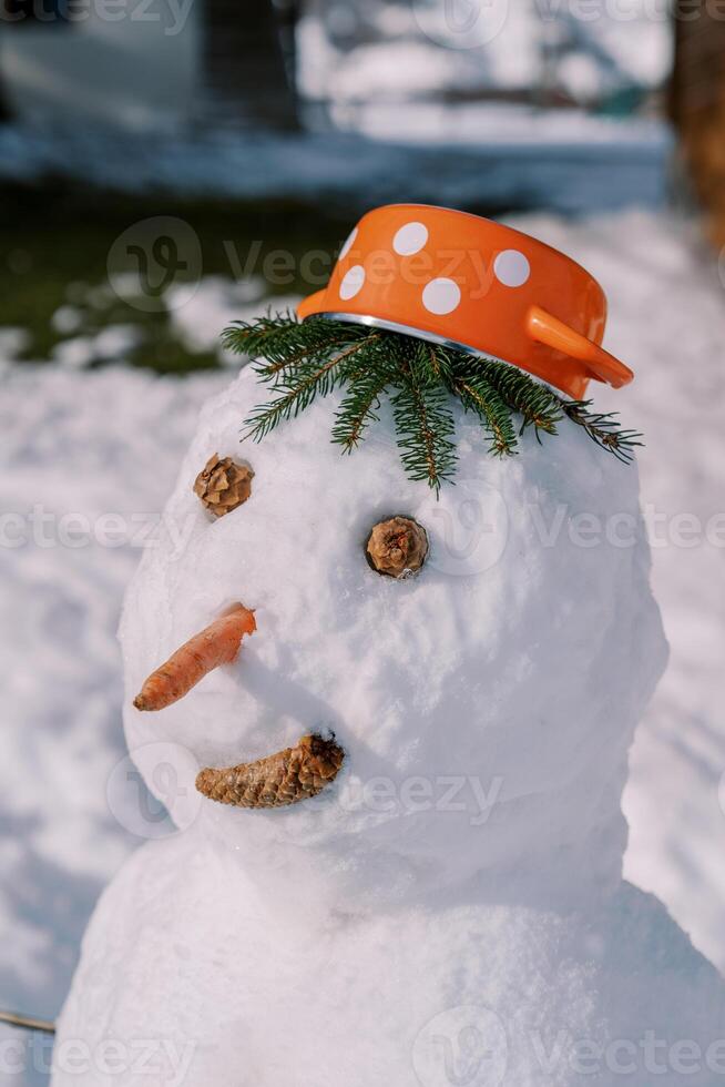 Smiling snowman in a saucepan hat stands in the courtyard photo