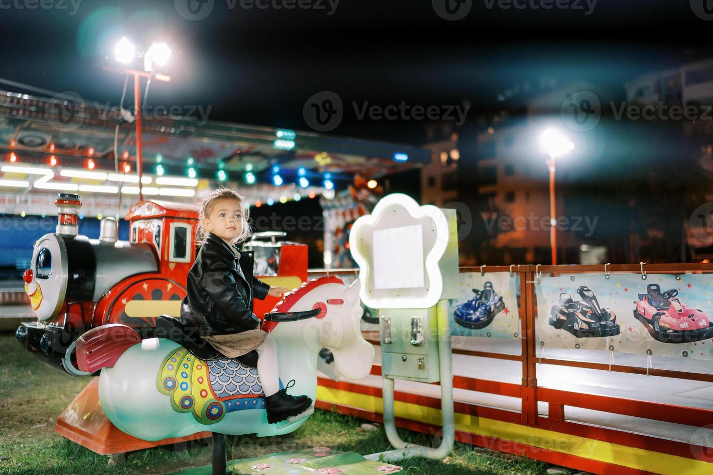 Little girl sits on an electric rocking horse swing at a fair and looks away photo