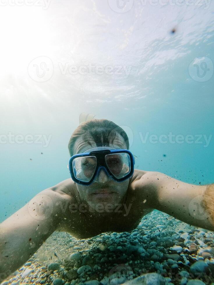 Diver in snorkeling goggles swims above the sea pebble bottom photo