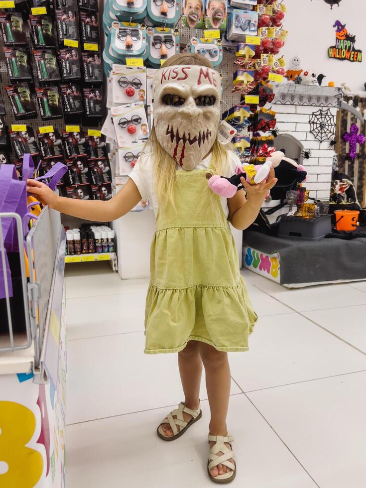 Podgorica, Montenegro - 14 august 2023. Little girl stands in a scary Halloween mask in a shop photo