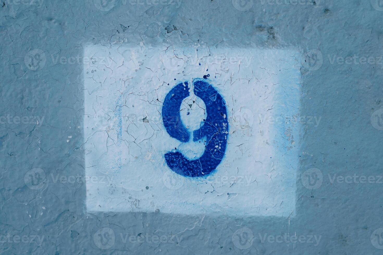 Number nine drawn on a scratched blue wall in a white rectangle photo