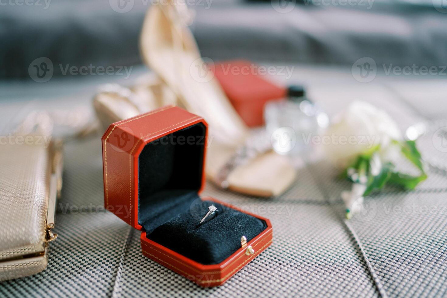 Wedding ring in a red box lies on the sofa next to the bride clutch photo