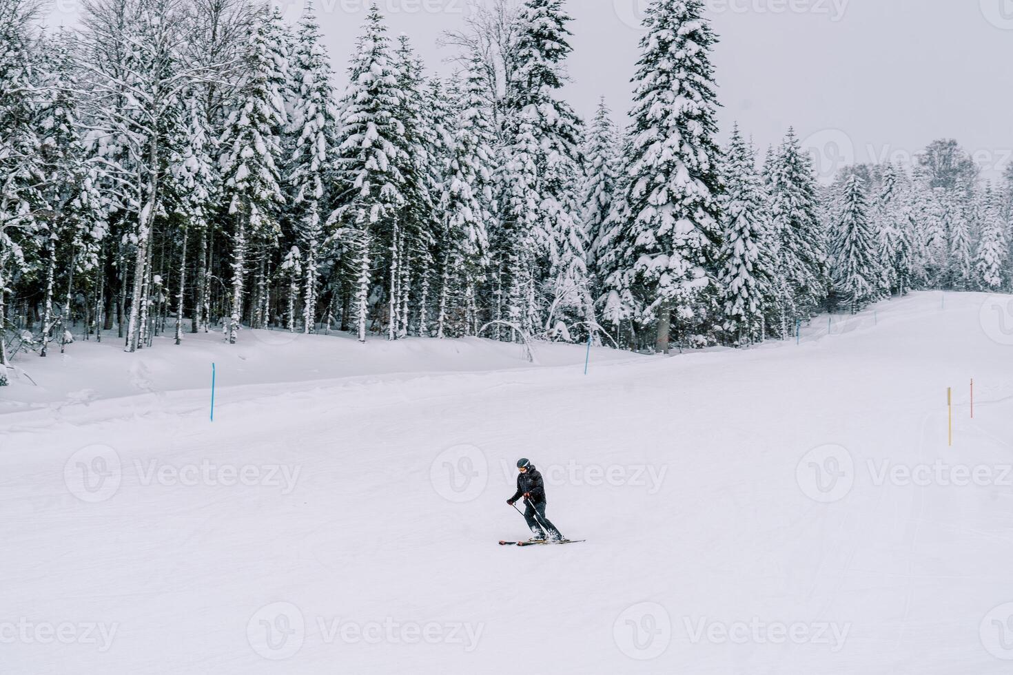 Skier in a ski suit rides leaning sideways along a snowy slope along the forest photo