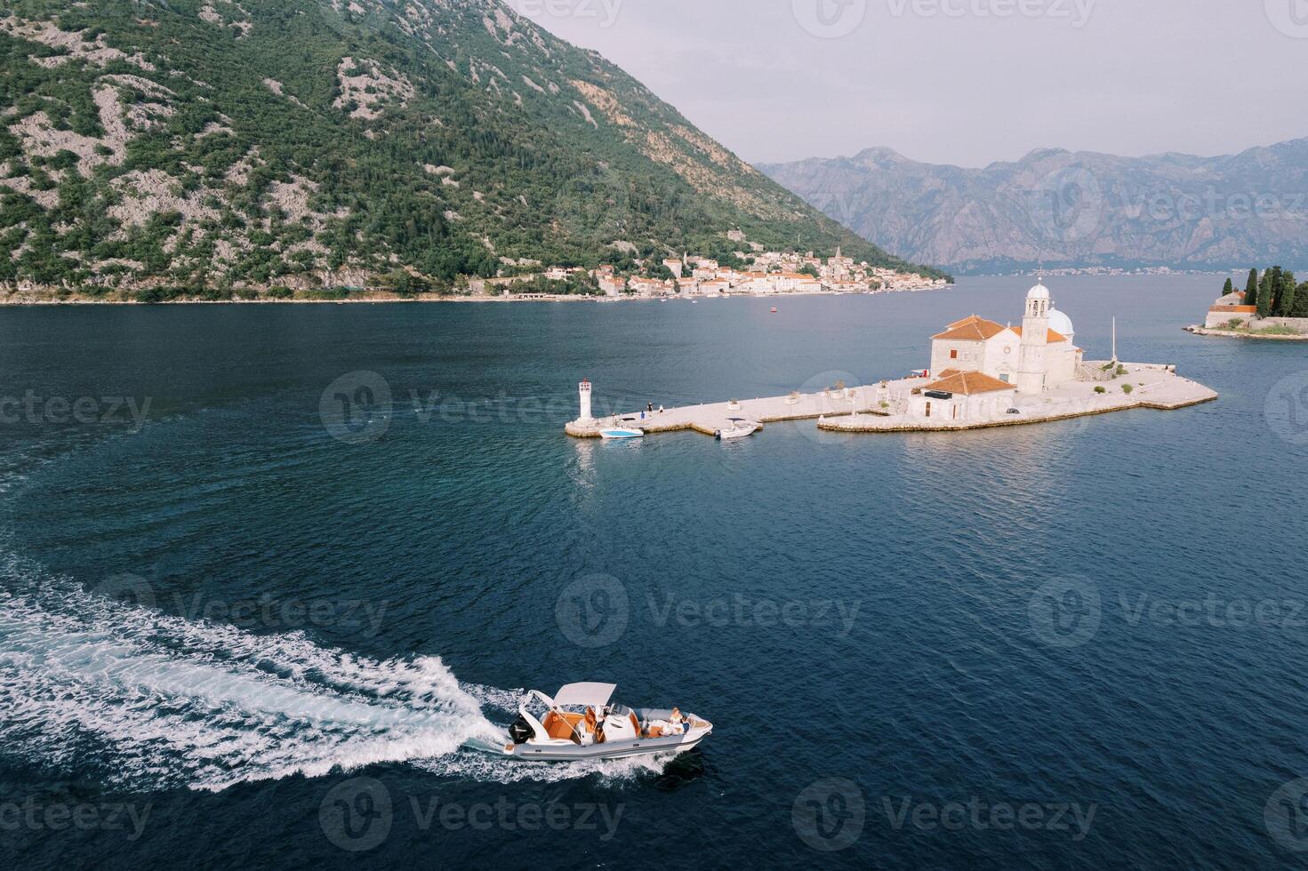 Motorboat sails on the sea past the Church of Our Lady on the Rocks of the island of Gospa od Skrpjela. Montenegro. Drone photo