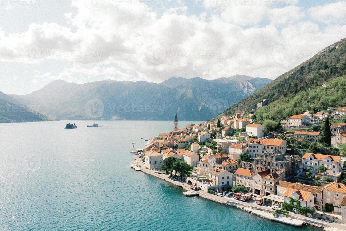 Ancient houses with red roofs on the shore of the Bay of Kotor at the foot of the mountains. Perast, Montenegro. Drone photo