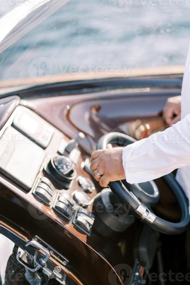 Captain steers a motor yacht with his hand on the steering wheel. Cropped. Faceless photo