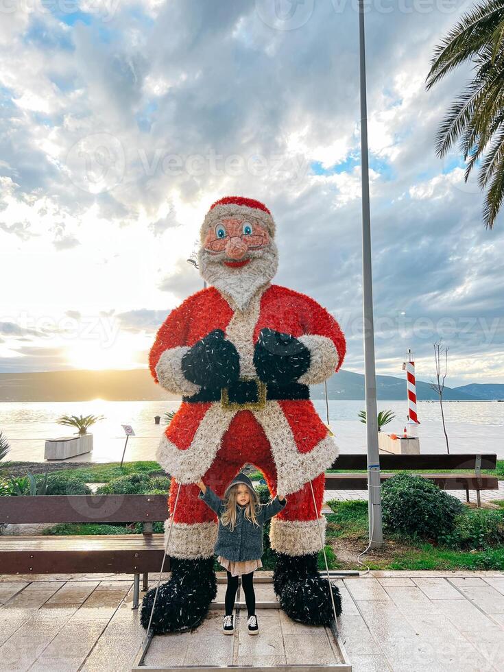 Little girl stands near the figure of Santa Claus on the promenade by the sea photo