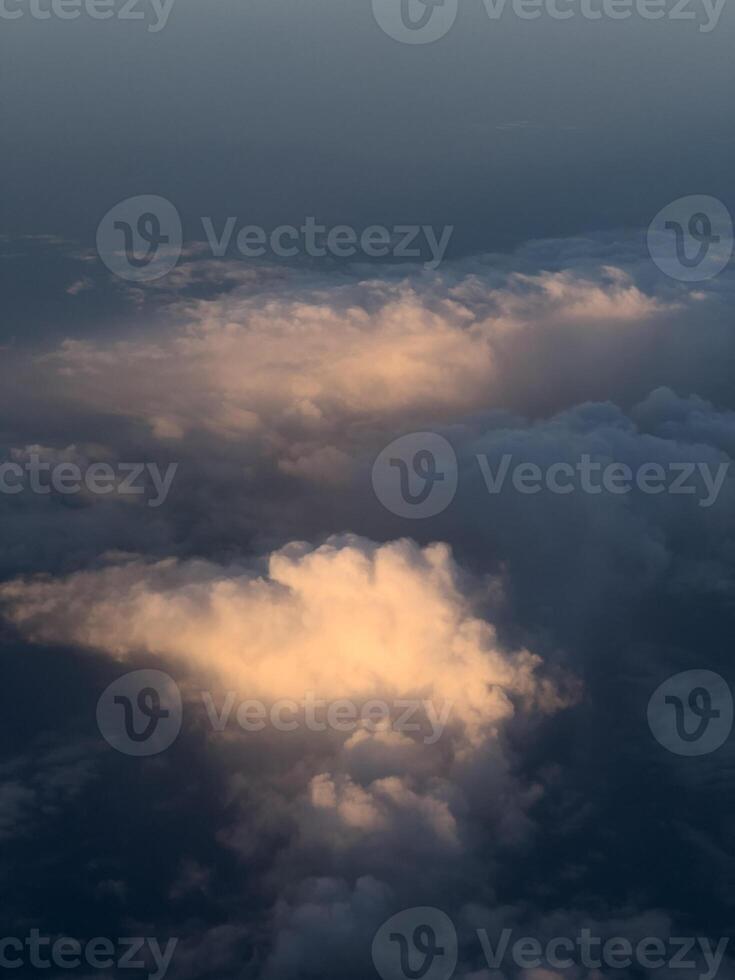 Porthole view of cumulus clouds in pink sunbeams on a dark blue background photo