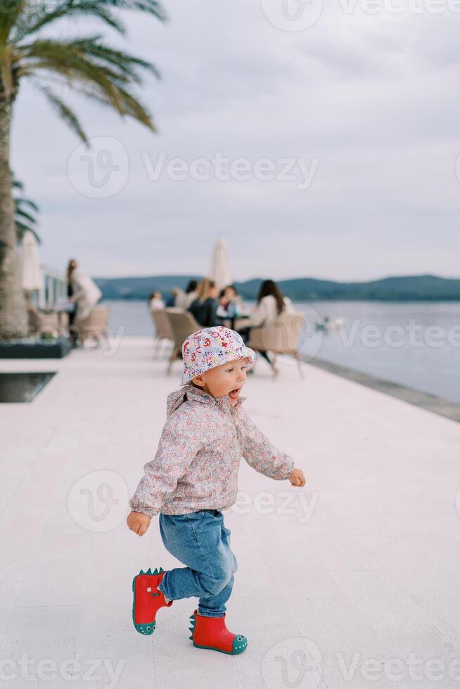 Little girl runs along the embankment by the sea, her mouth open photo