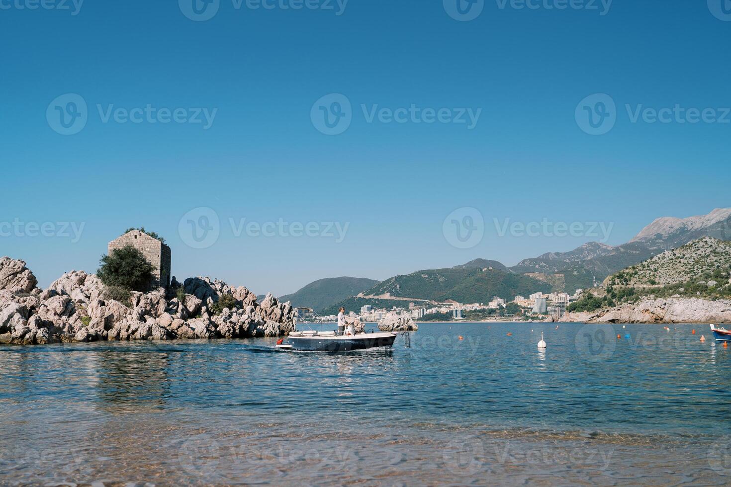 Man sails a fishing boat past an island off the mountainous coast. Przno, Montenegro photo