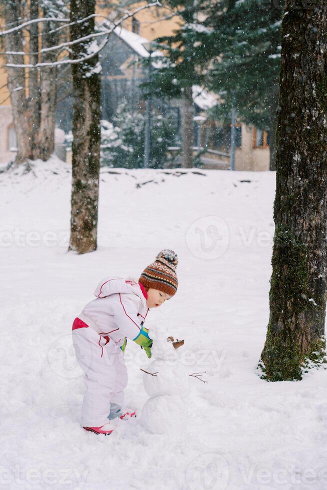 Little girl makes a snowman under snowfall in the forest photo