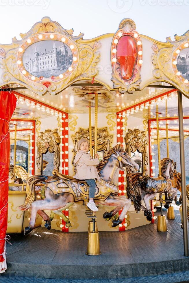 Little smiling girl rides a toy horse on a colorful carousel in a square photo