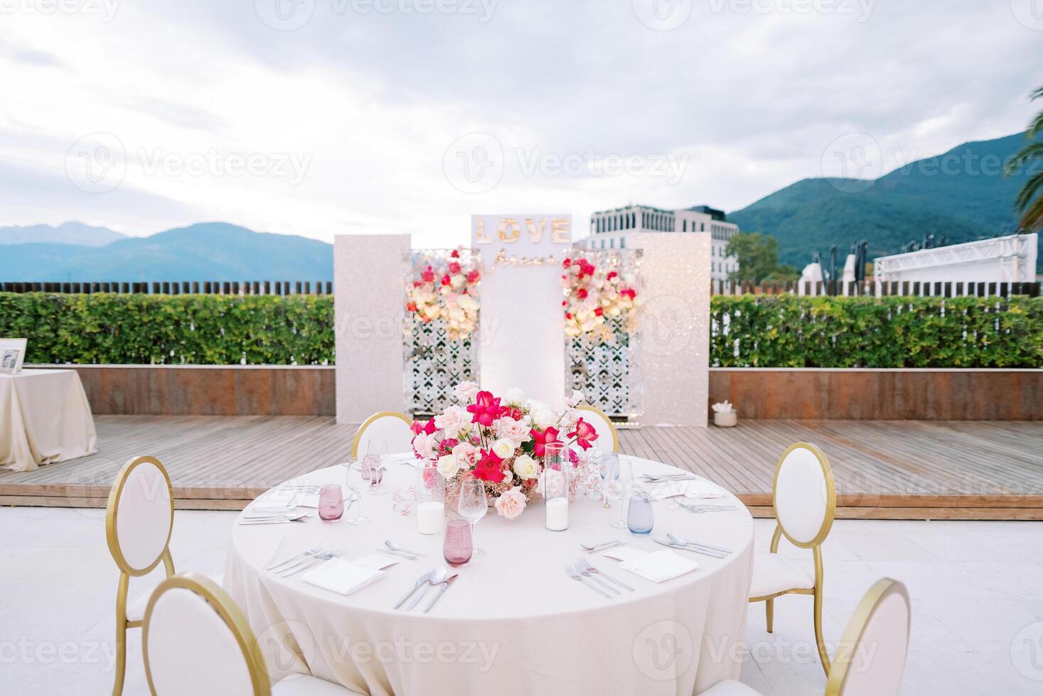 Round festive table with chairs stands opposite a stand with bouquets of flowers. Caption. Love forever photo