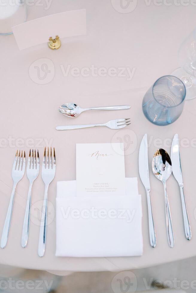 Personalized invitation lies in a white napkin on the table next to the cutlery, opposite a blank card on a stand photo