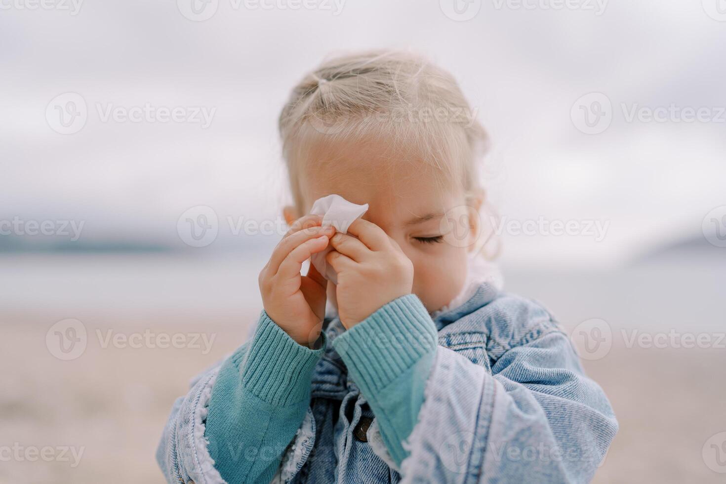 Little girl with closed eyes wipes her forehead with a napkin photo