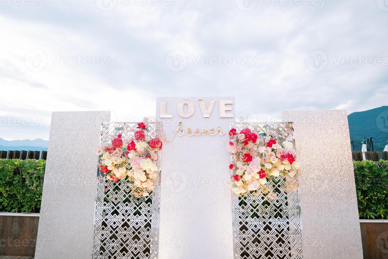 White photo zone stand with colorful bouquets of flowers. Caption. Love forever