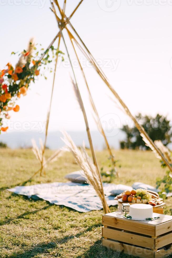 Boxes with festive treats stand near the wedding tipi arch on a green lawn photo
