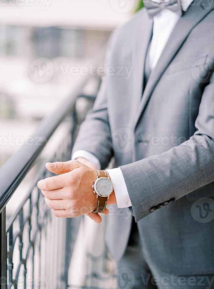 Groom in a suit fastens his watch strap while standing on the balcony. Cropped. Faceless photo