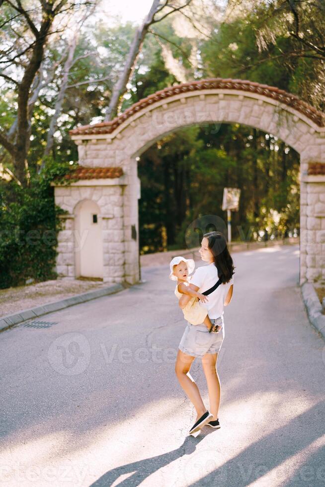 Mother with a little girl in her arms walks along the road in the park photo