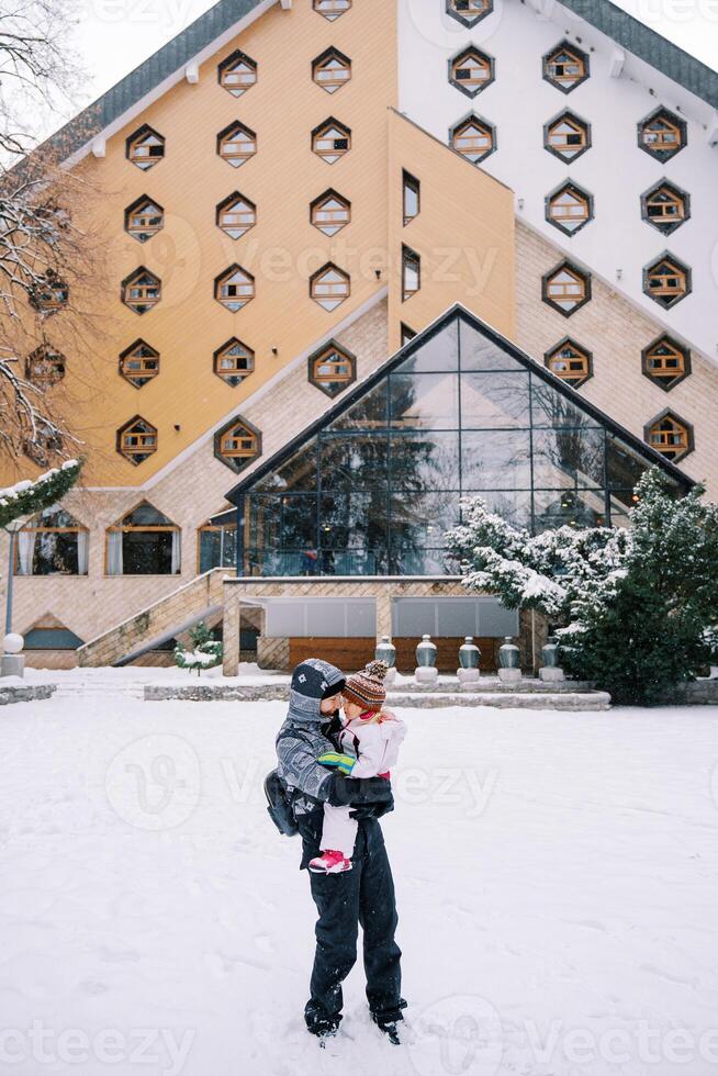 Mother with a little girl in her arms stands in front of a triangular hotel in the snow photo