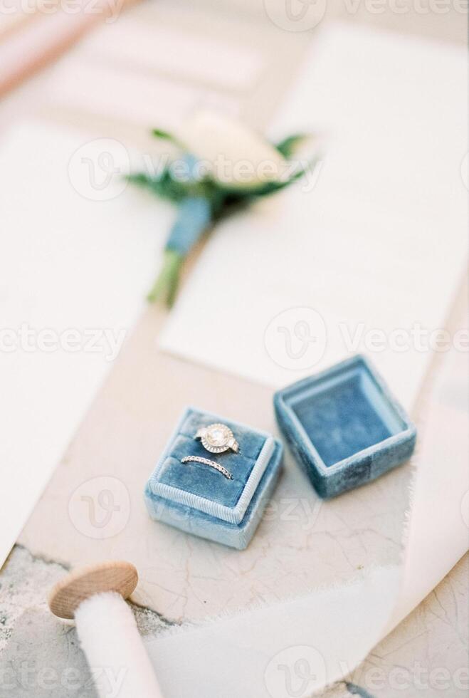 Wedding rings lie in a box on the table near the invitations and a white ribbon on a reel photo