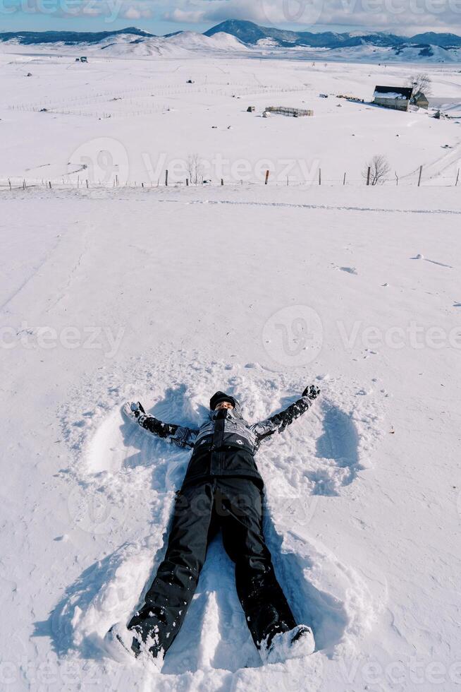 Young woman in a ski suit makes a snow angel in the snow photo