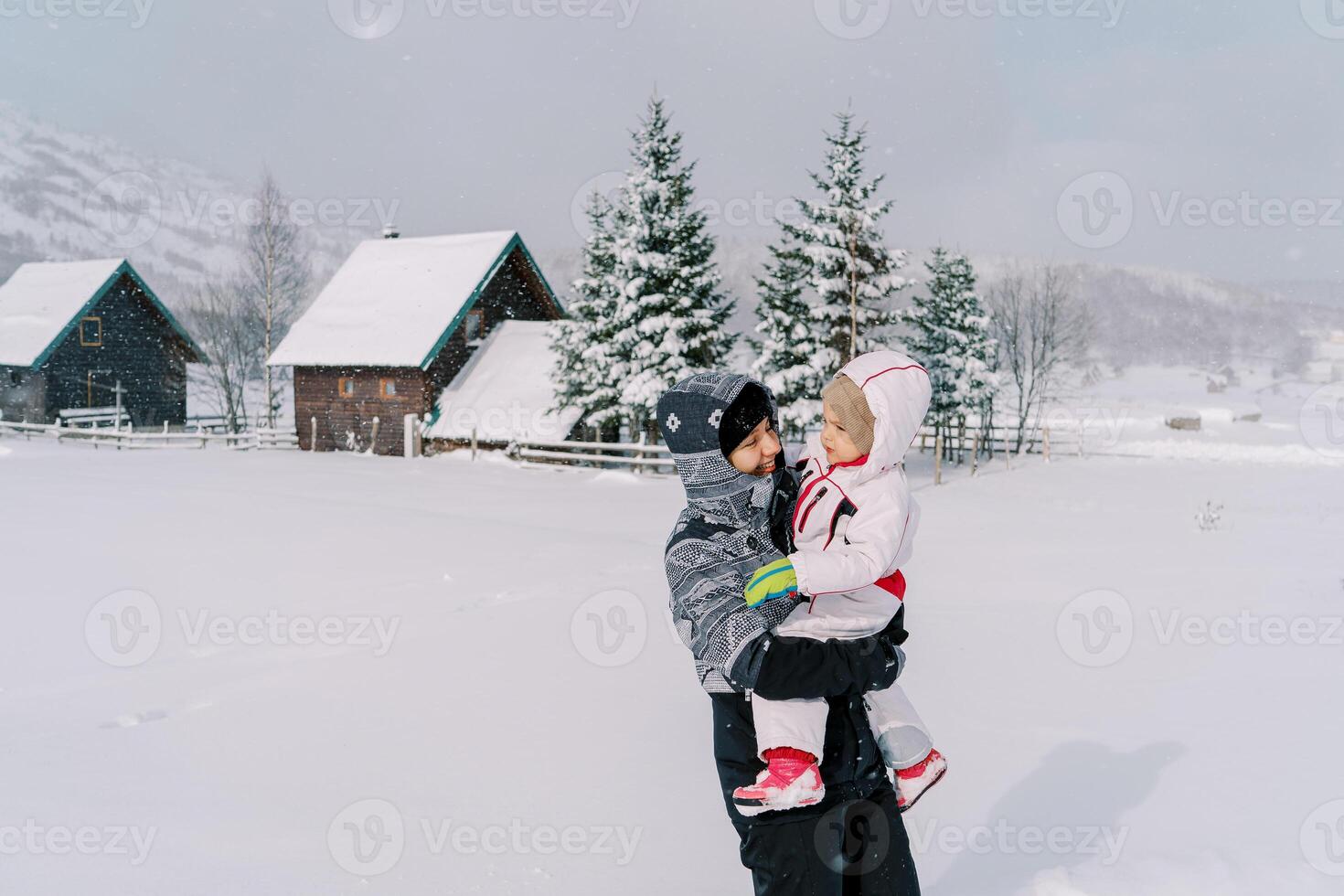 mamá mira a un pequeño niña en su brazos mientras en pie en un Nevado pueblo en un montaña Valle foto