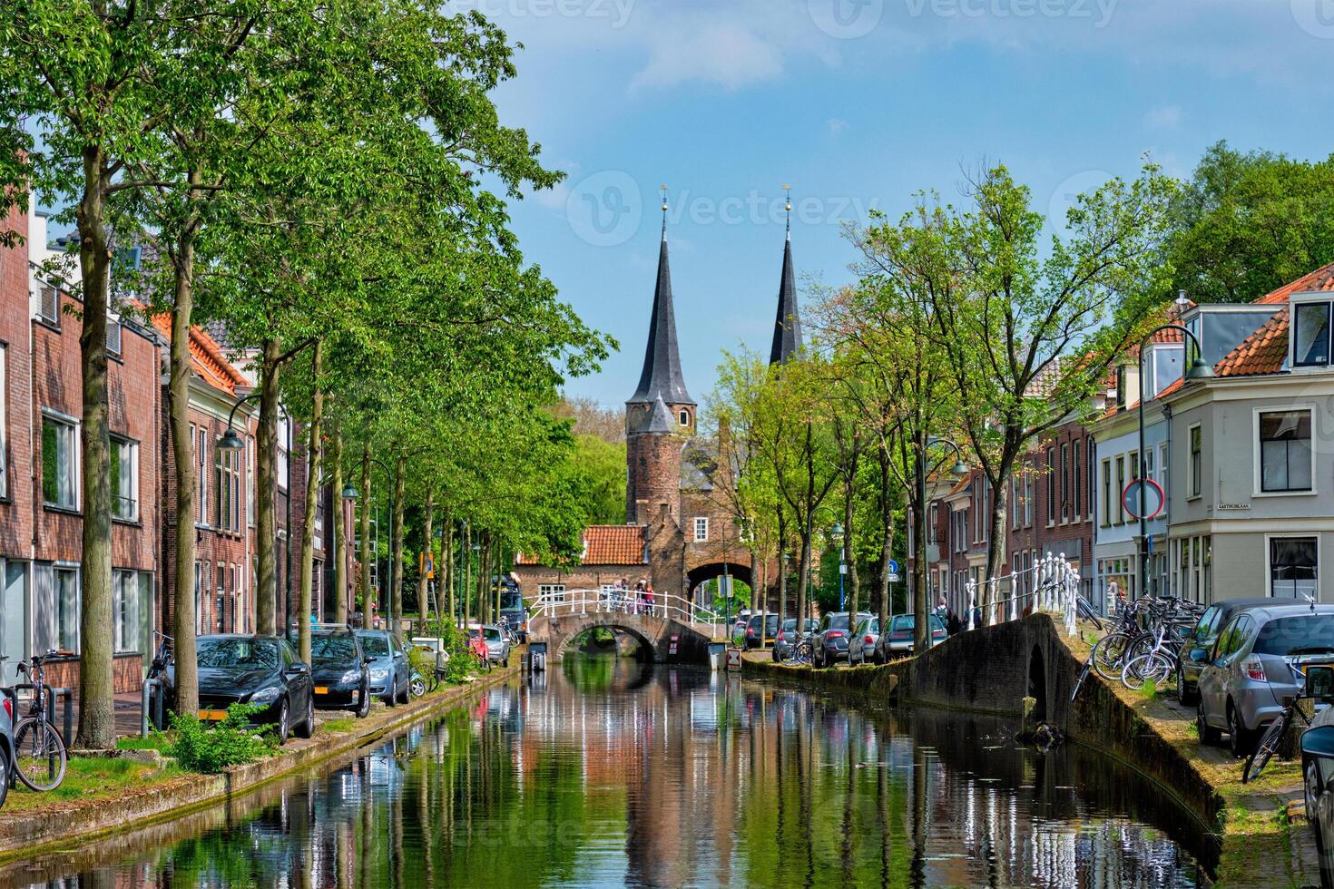 Delft cityscape view with Eastern Gate Oostport and canal with cars and bicycles parked along photo