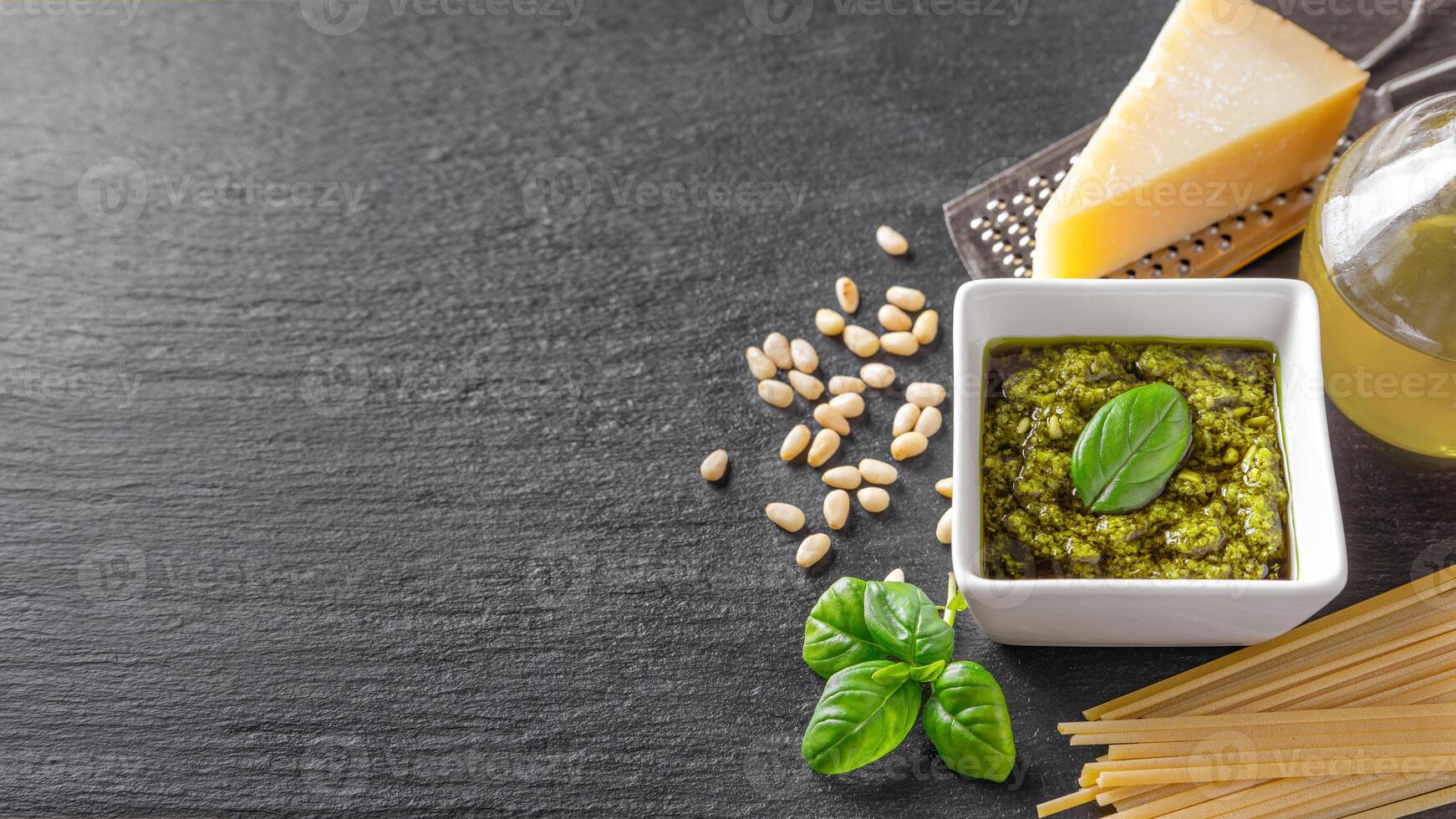 Homemade pesto sauce in small square jar and ingredients for pasta on black slate background photo