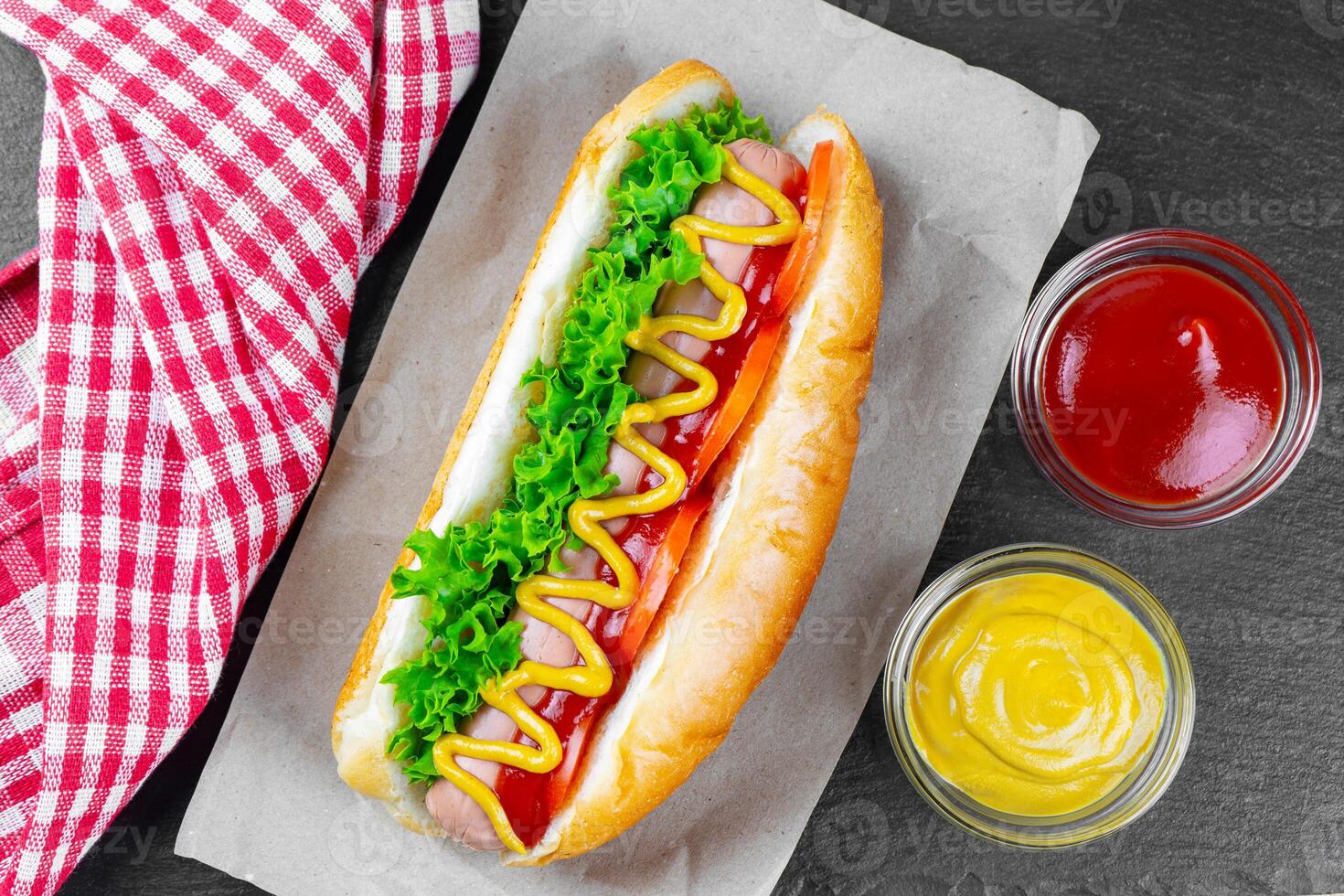 Homemade Hot Dog with mustard, ketchup, tomato and fresh salad leaves on black slate background photo