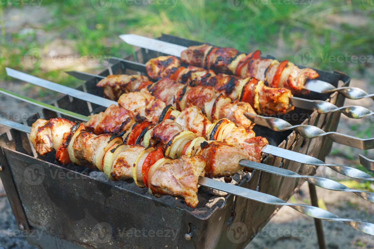 Grilled pieces of meat on skewers, shish kebab with vegetables, cooking process on brazier photo
