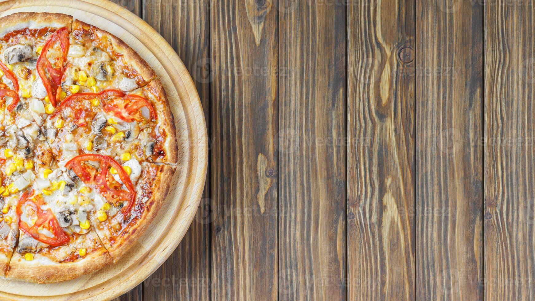 Italian pizza with melted mozzarella cheese mushrooms, corn and tomato on brown wooden background. photo