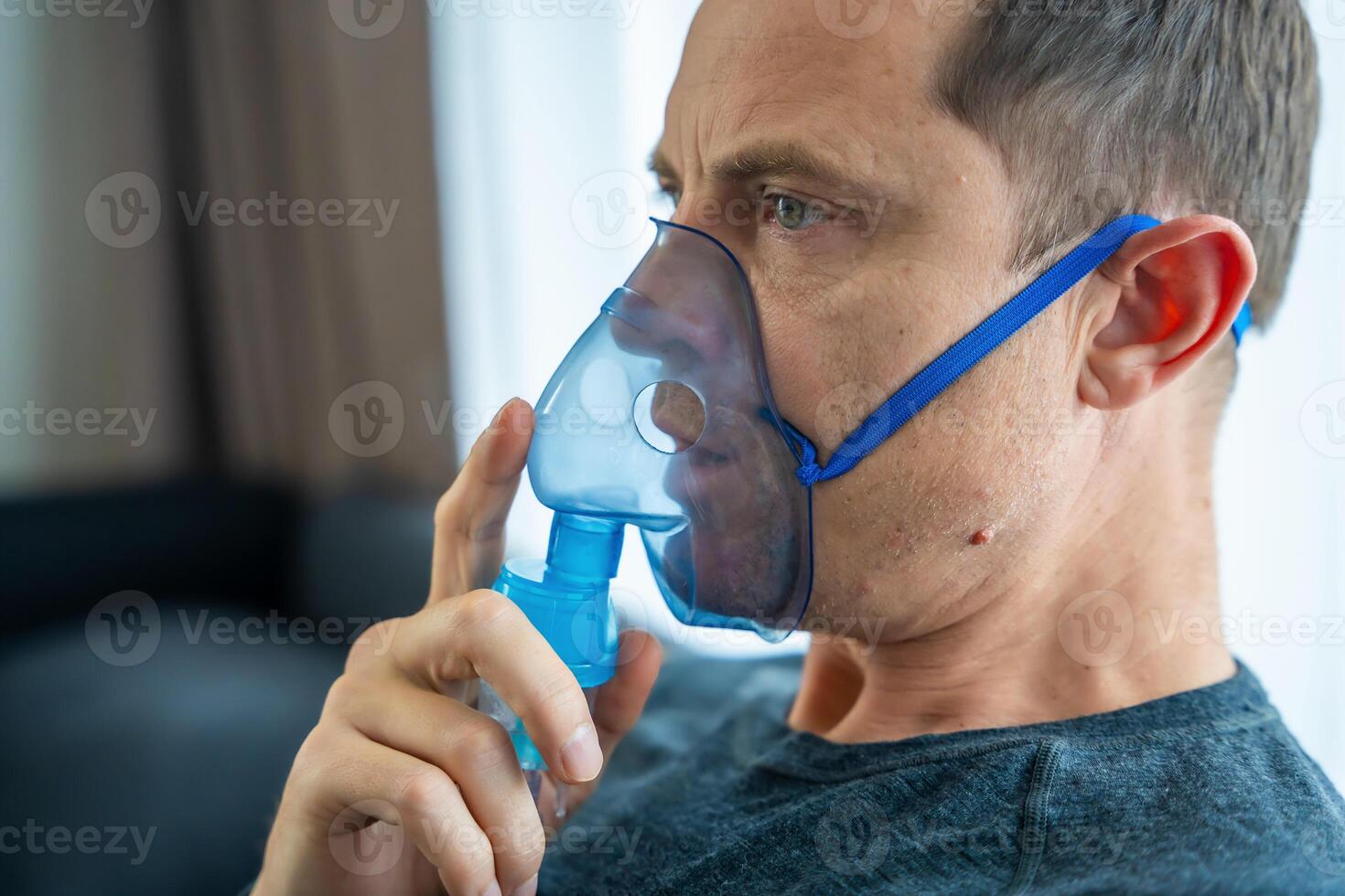 Unhealthy man wearing nebulizer mask in home. Health, medical equipment and people concept. High quality photo