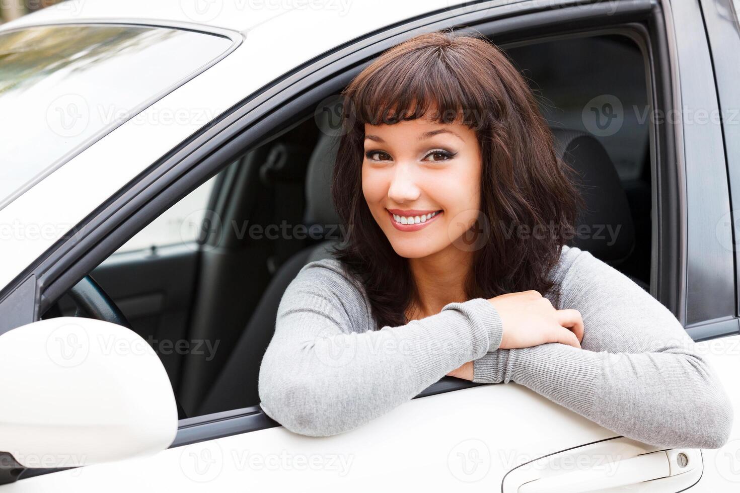 Happy owner of a new car. Young pretty woman driver smiling to you photo