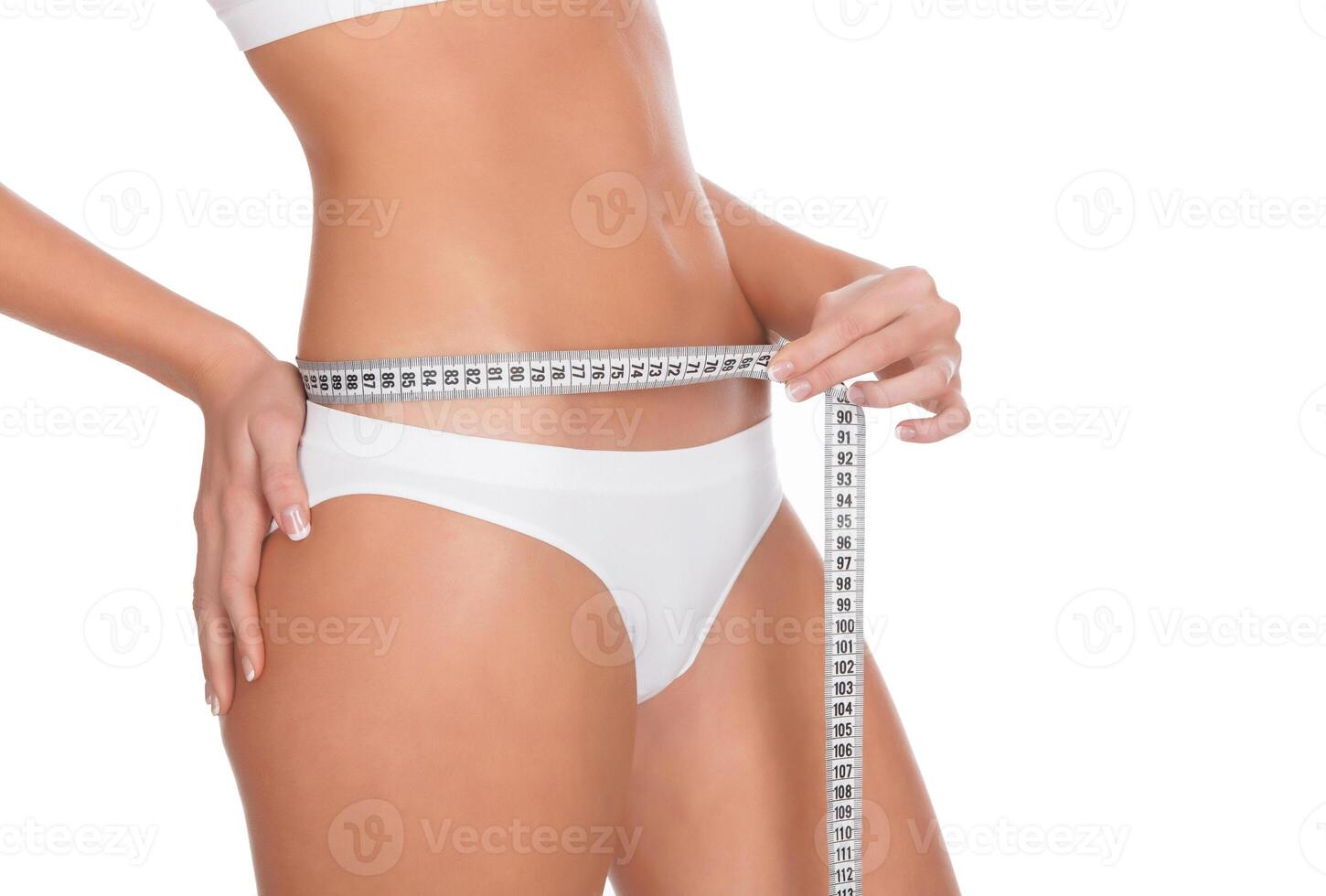 Mujer joven en forma midiendo su cintura, fondo blanco. foto