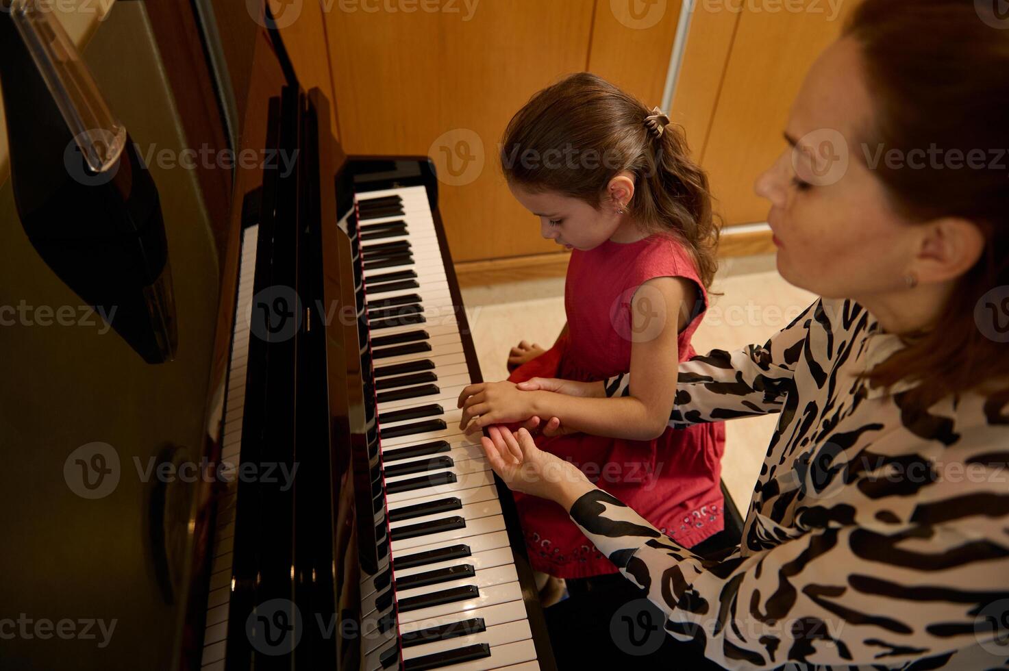 pequeño niño niña teniendo un piano lección con su maestro. hembra pianista explicando el correcto posición de manos en piano llaves. musical educación y talento desarrollo en progreso. parte superior ver foto