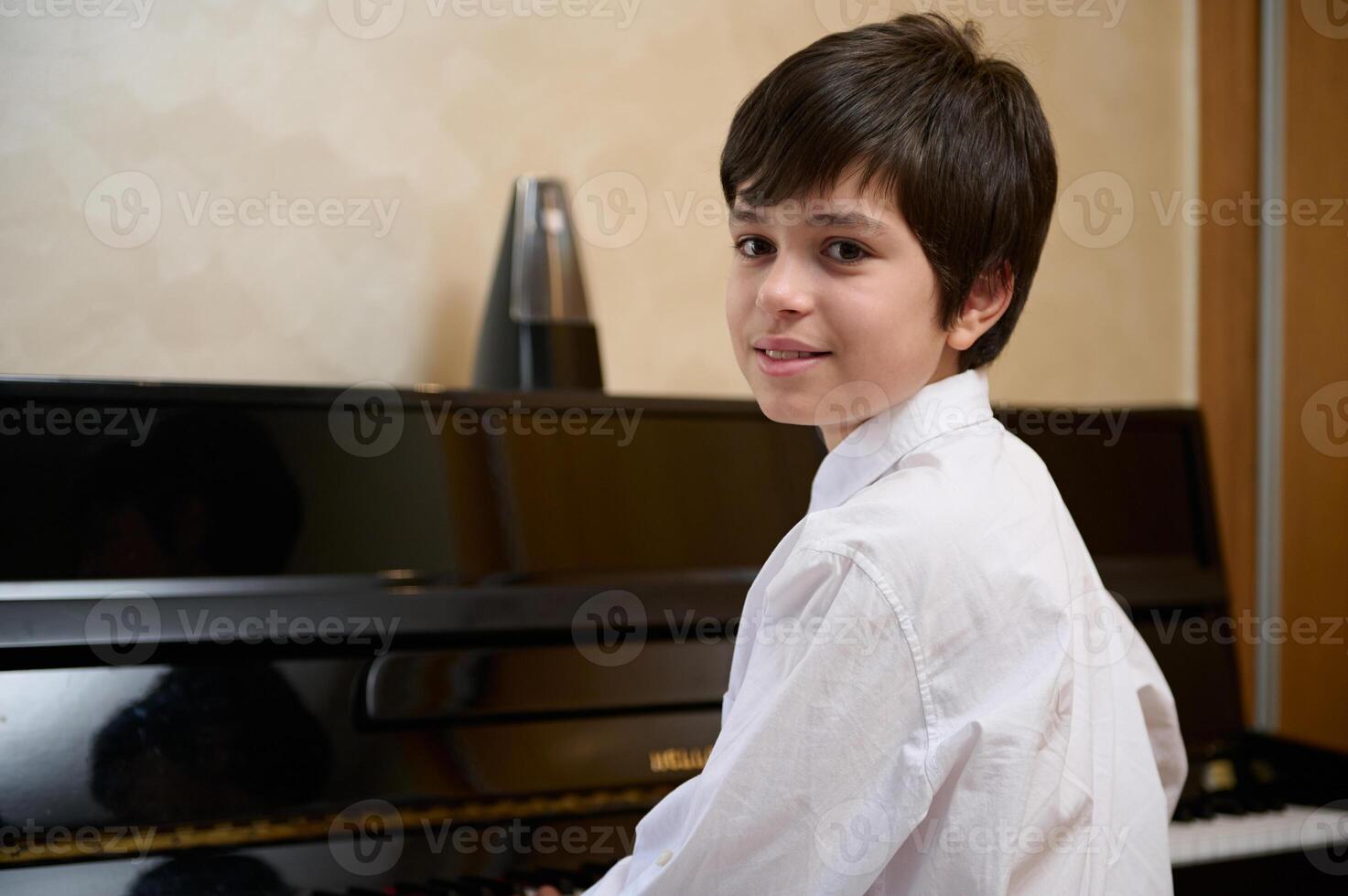 Close-up portrait of a multi ethnic teen boy, little pianist musician smiling looking at camera, sitting at piano forte photo