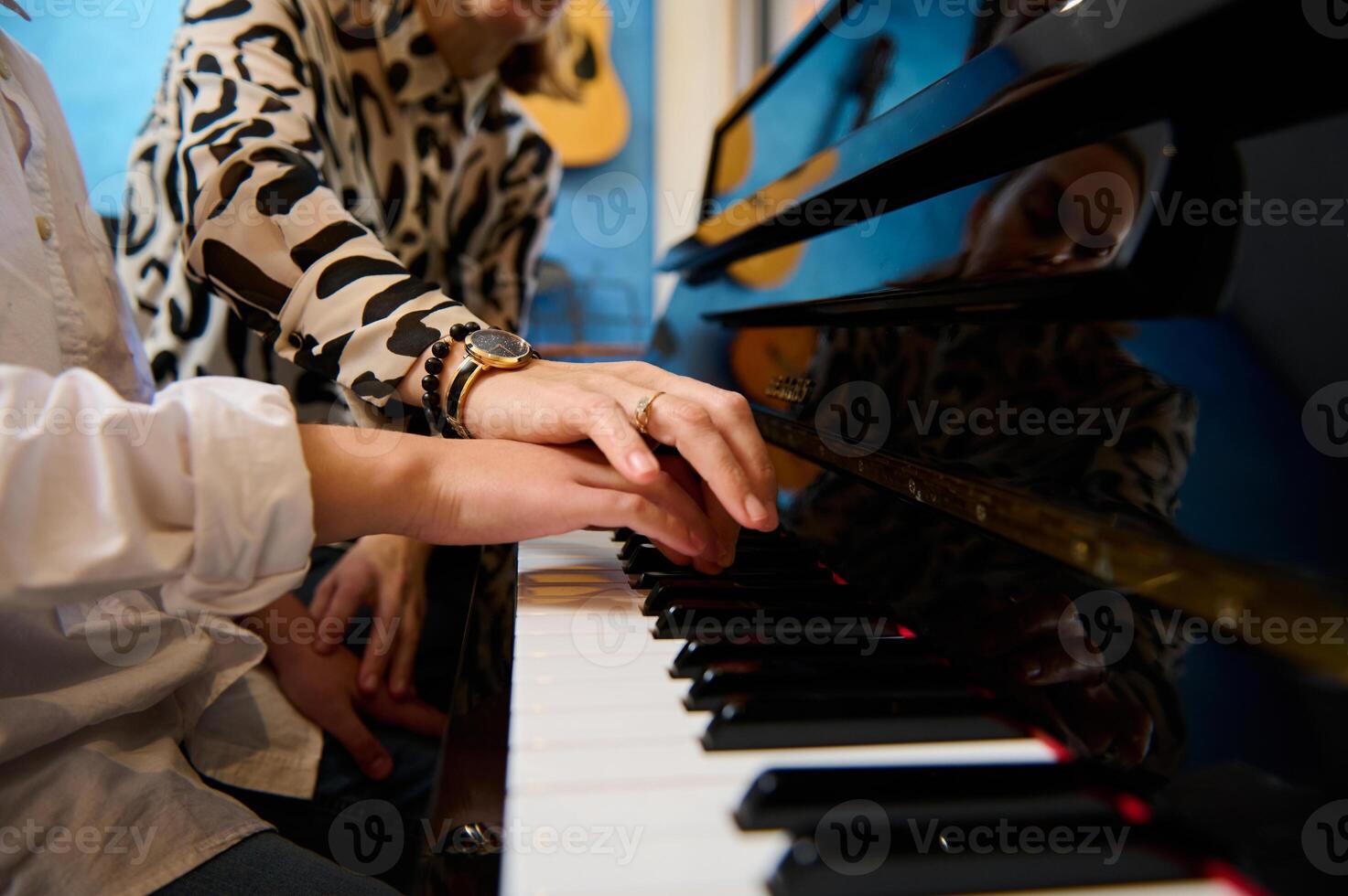 Female musician pianist teaching a teenager boy the correct position of fingers, sitting at piano while performing musical composition on grand pianoforte, during music lesson. Closeup photo