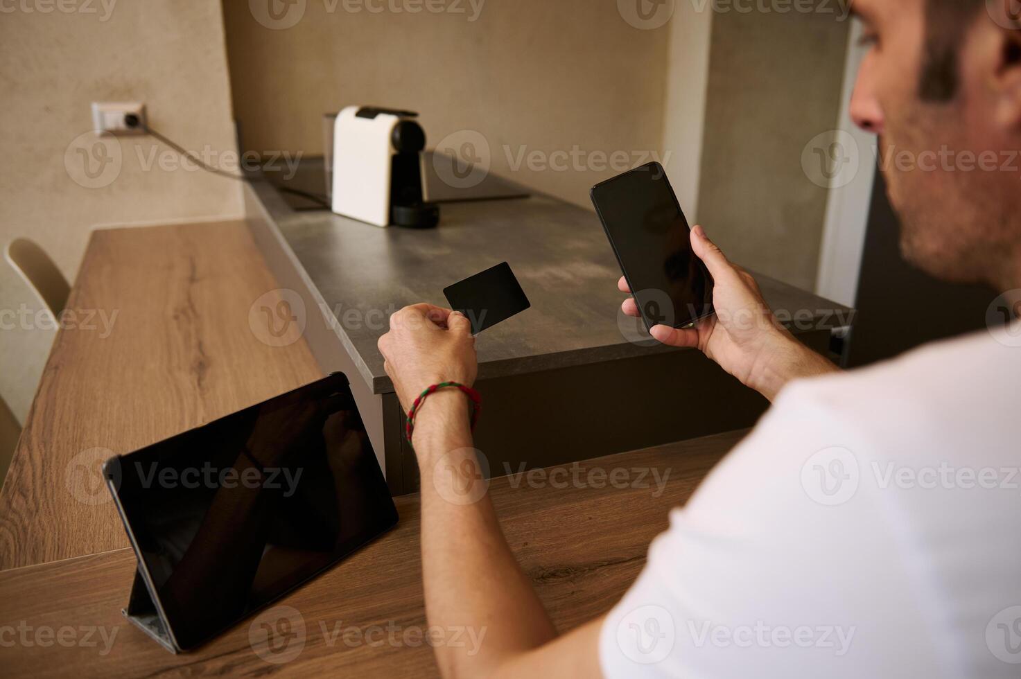 Rear view of young adult man holding a blank black credit card and smartphone with empty mockup digital screen photo