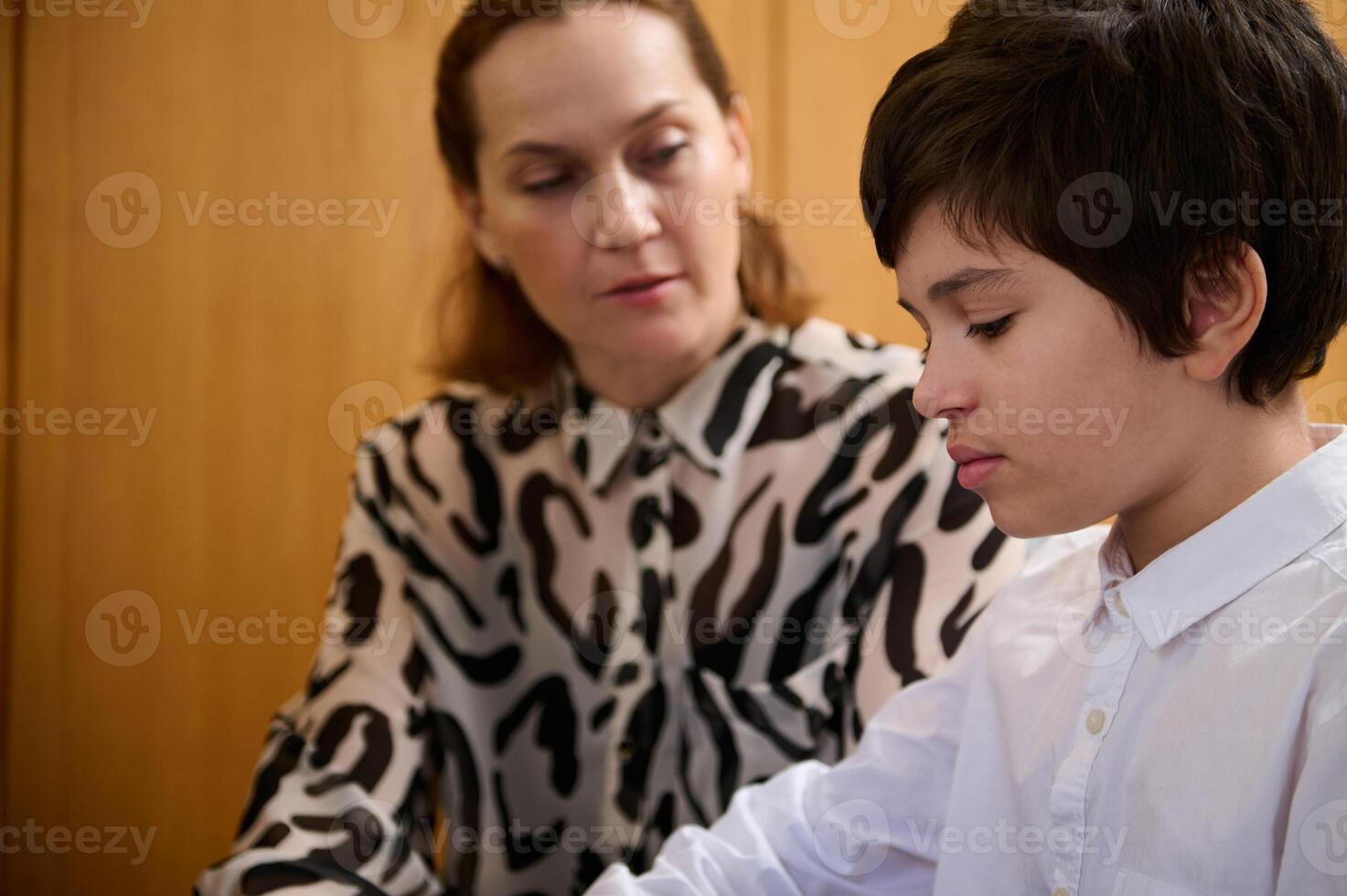 Teenager boy pianist musician practicing piano, playing classical melody, sitting near his music teacher while an individual lesson photo