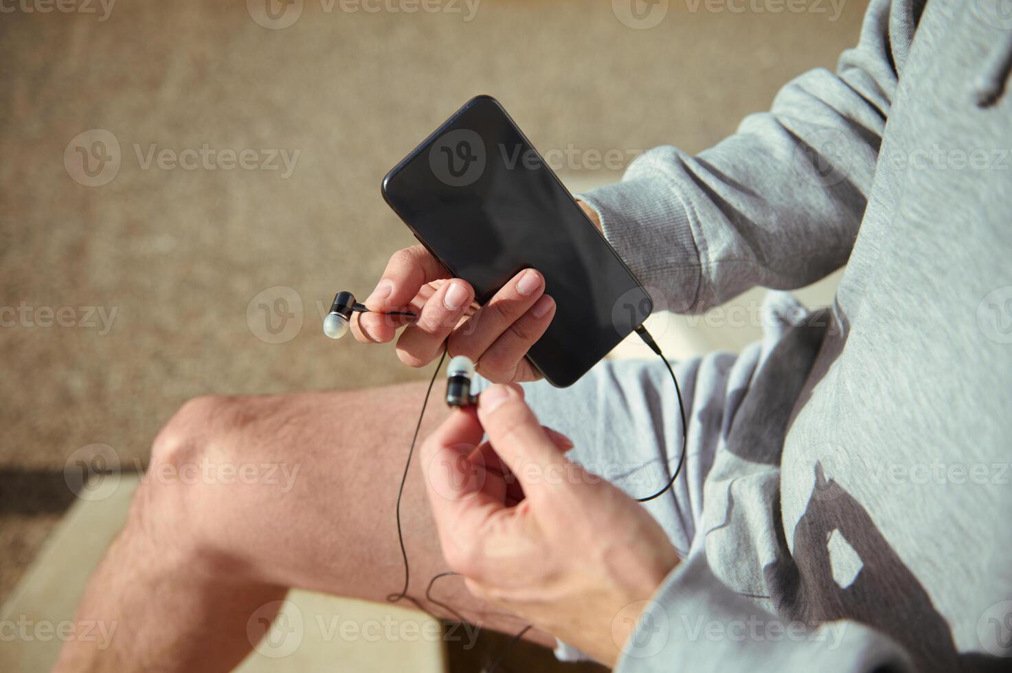 Athlete hands holding earphones and smartphone with black blank mockup screen. Copy space for ad or fitness application photo