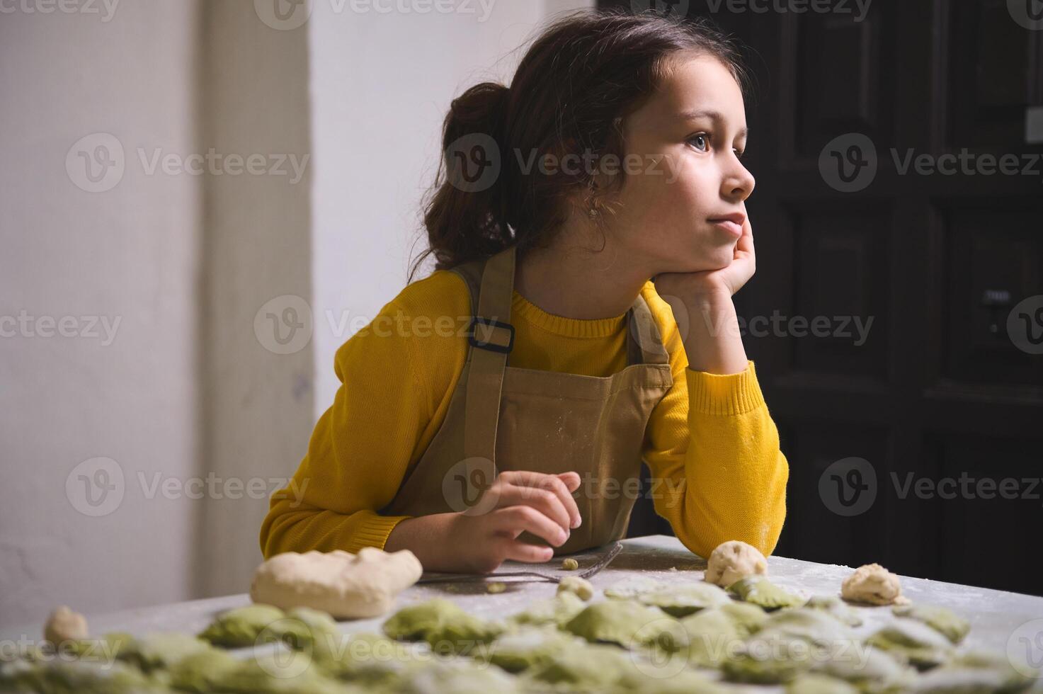 hermosa pequeño niña soñando mirando lejos, en pie a enharinado mesa con moldeado albóndigas niños Cocinando clase. culinario. contento infancia foto