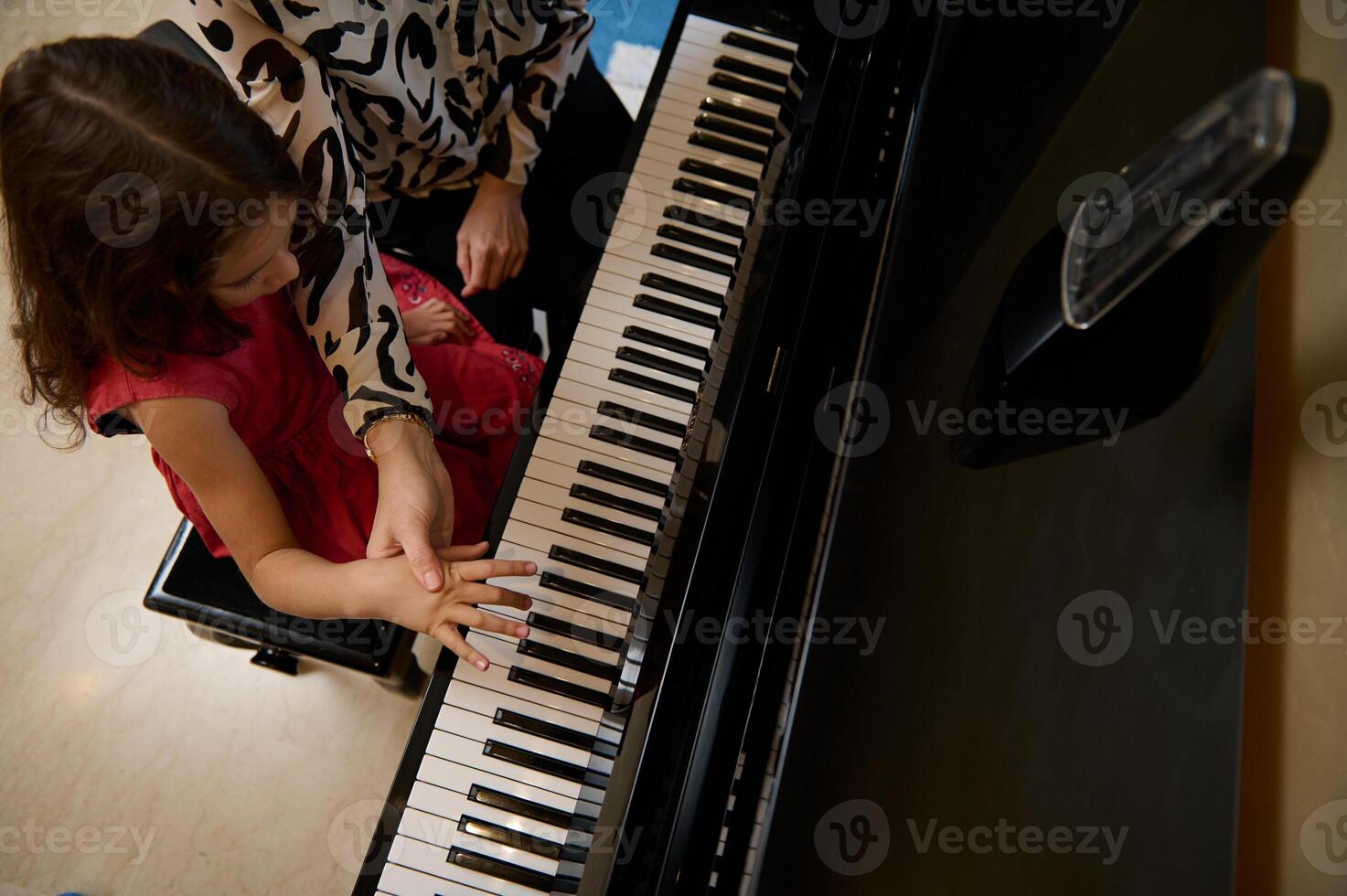 Overhead view pianist explaining to a little kid girl the correct position of fingers on the black and white piano keys. Caucasian cute child girl plying grand piano under the guidance of her teacher photo