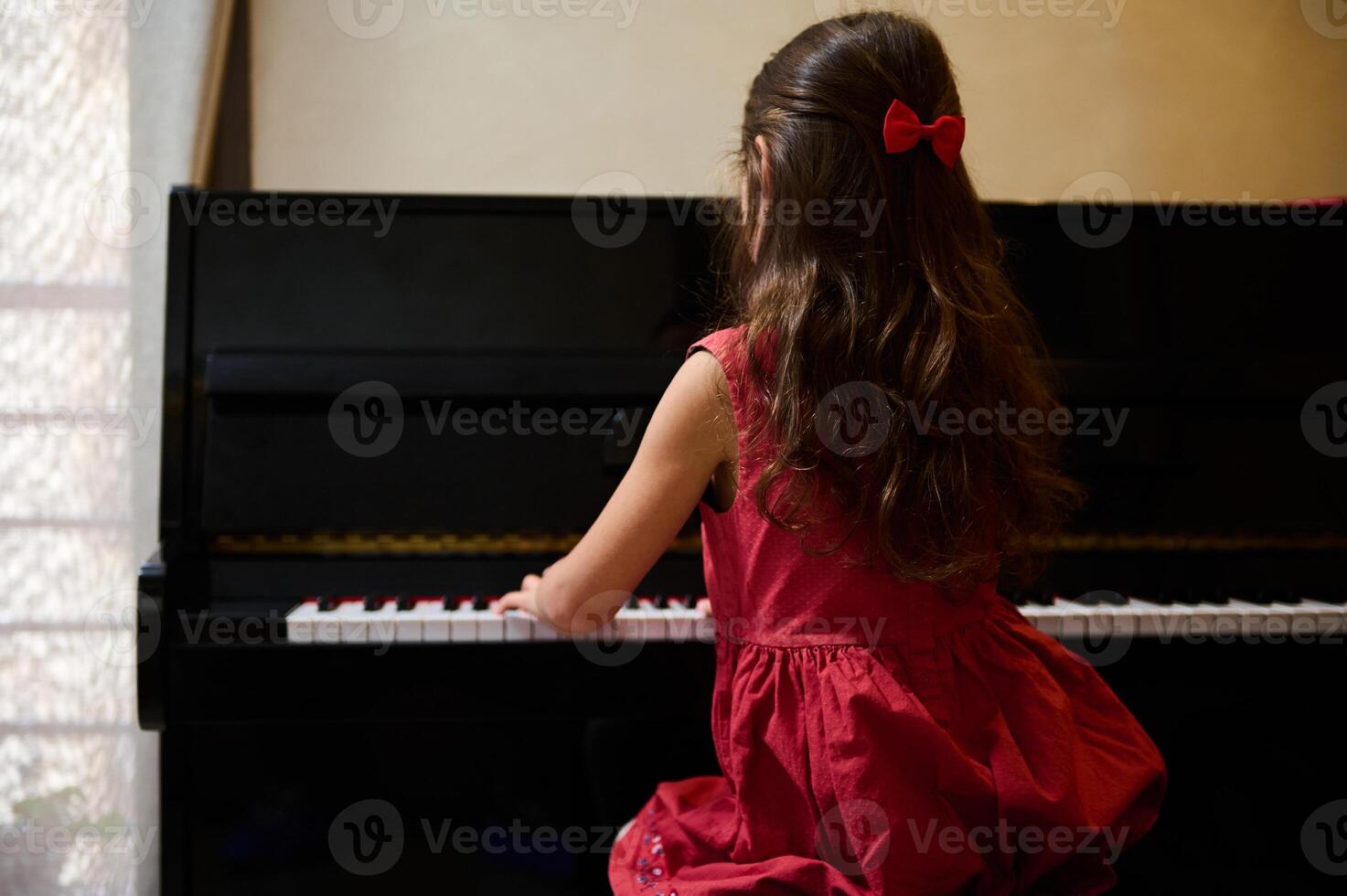 Back view of a cute child girl, a pianist student, future musician pianist touching the white keys with his fingers to create the rhythm of the melody, enjoying playing grand piano during music lesson photo